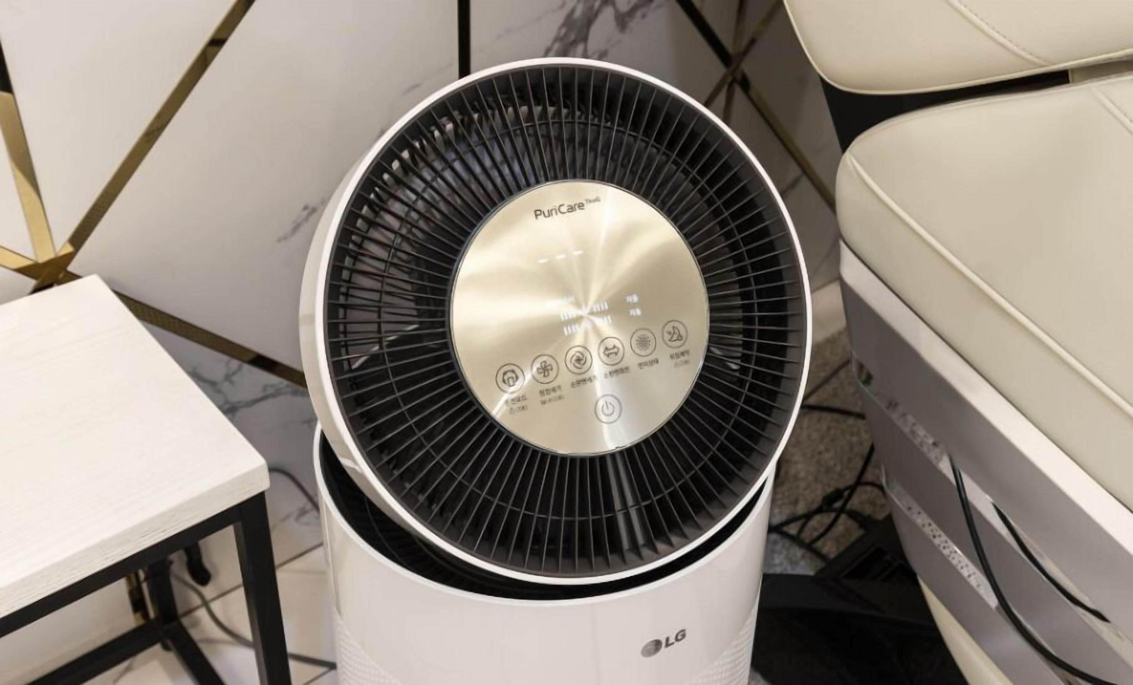 A white LG air purifier with a black fan and control panel, placed on a white table in a room with a marble floor and a white sofa.