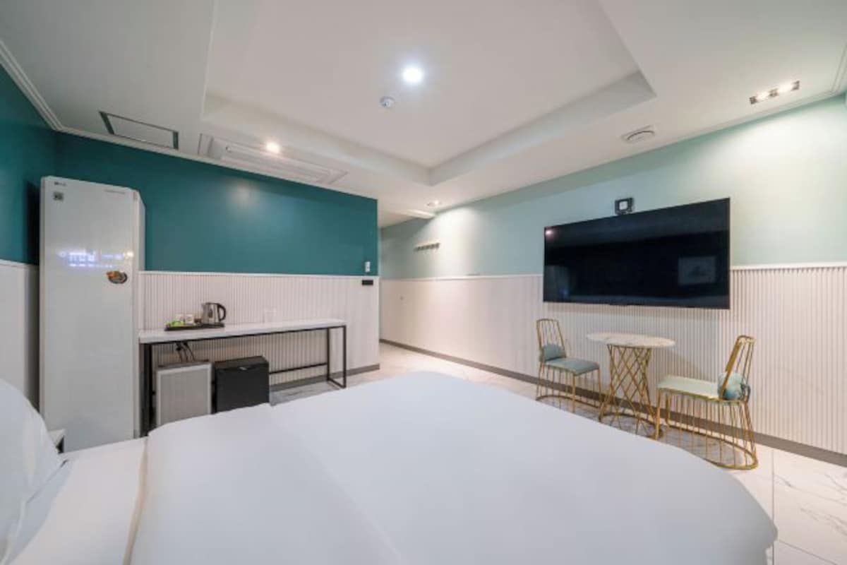 Una habitación de hotel con una cama, un escritorio con una silla, un televisor montado en la pared y una pequeña mesa con dos sillas.