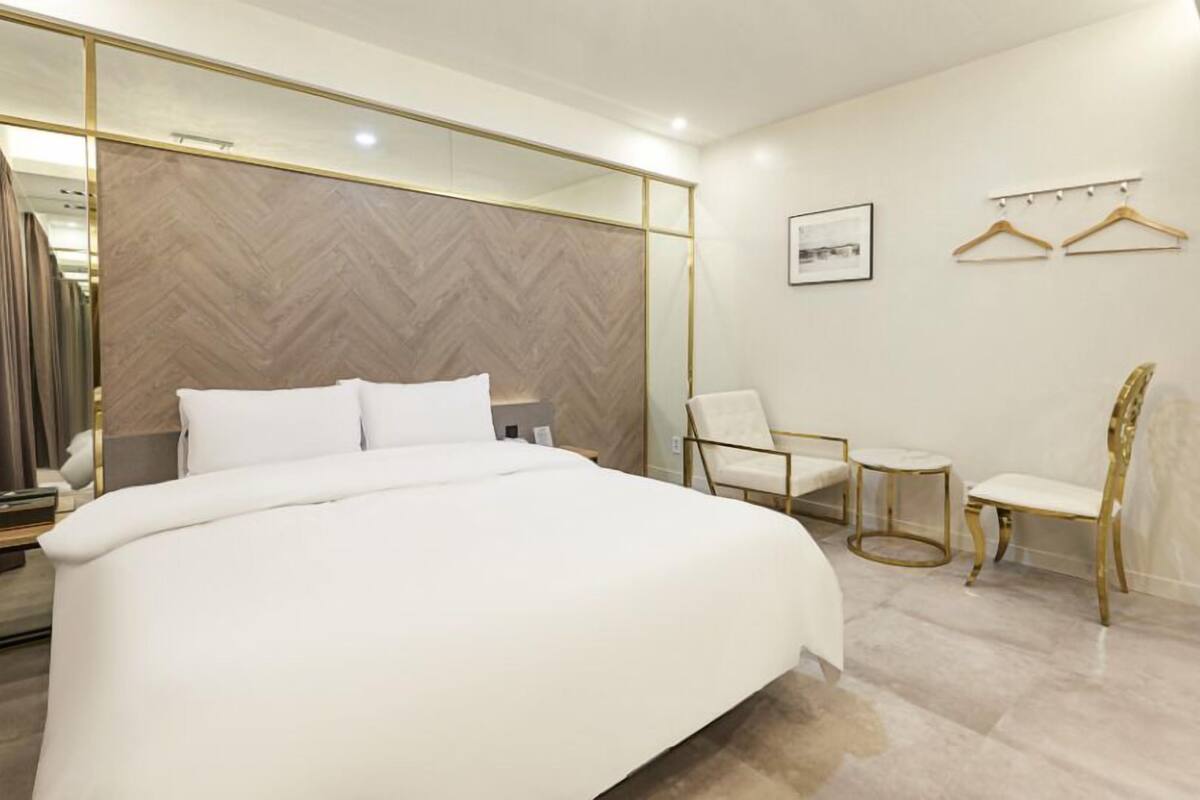A modern hotel room with a large bed, a chair, a small table, and a mirror.