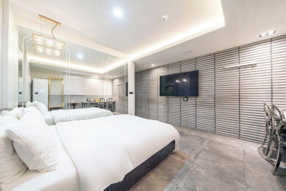 A modern bedroom with a large bed, a flat-screen TV mounted on the wall, and a minimalist design.