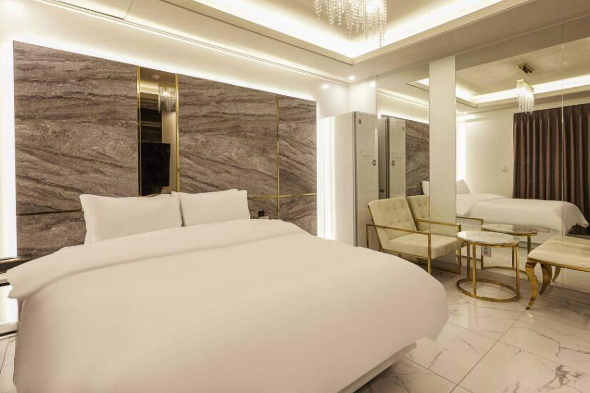 A modern hotel room with a large bed, a sitting area with a small table, and a mirror.