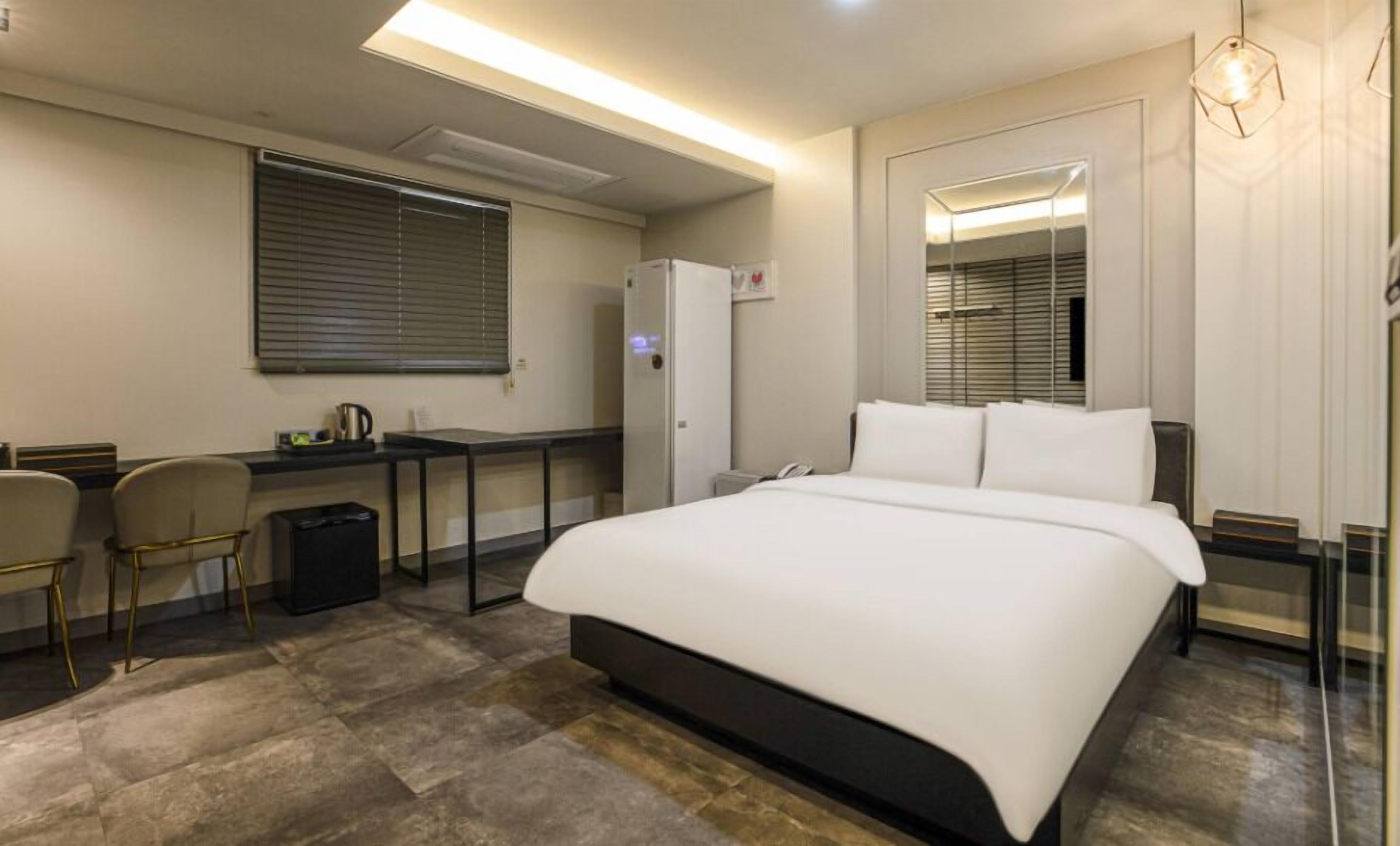 Una camera d'albergo con un letto grande, una scrivania con una sedia, un frigorifero e una finestra con tende.