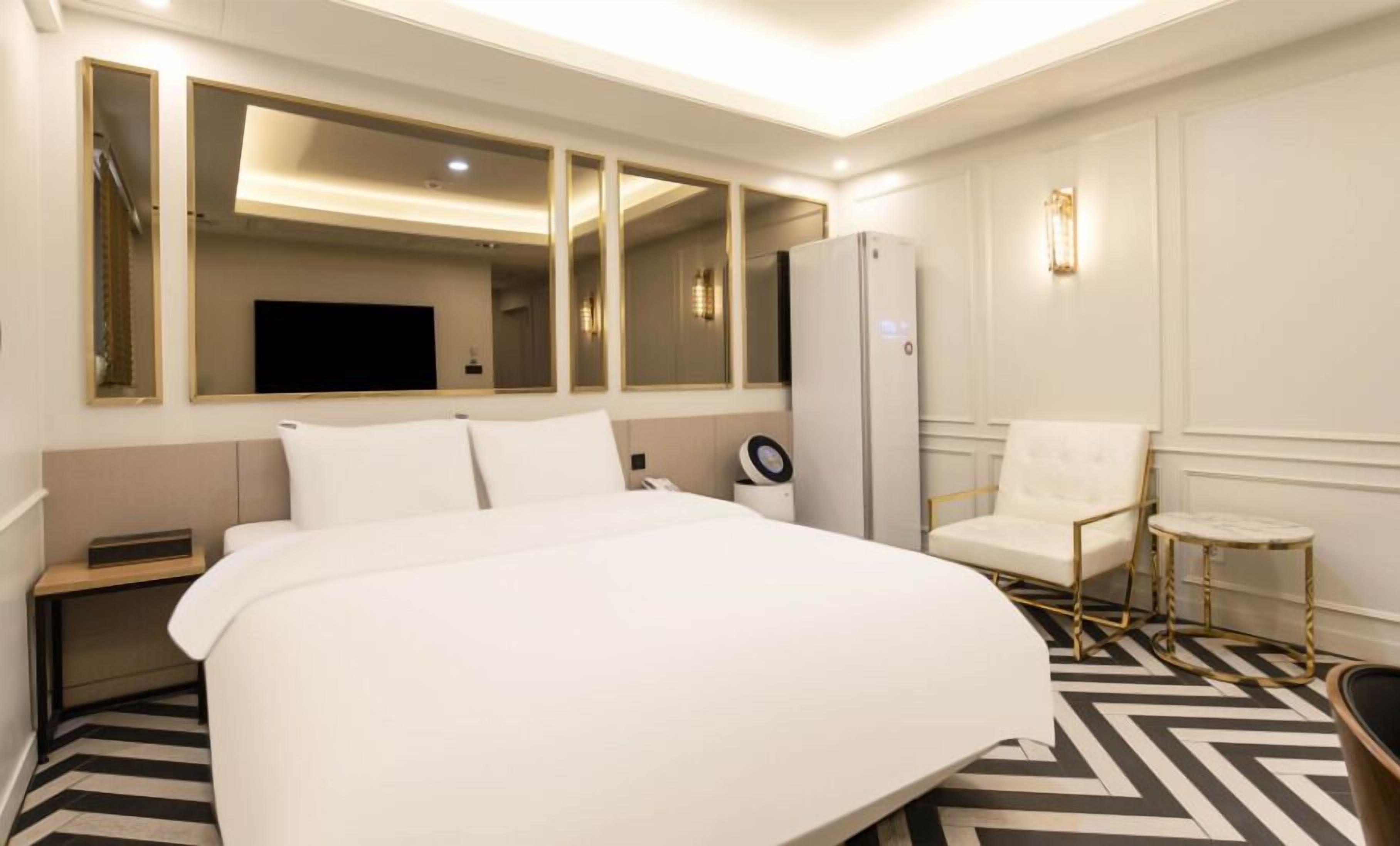 A hotel room with a large bed, a desk, a chair, a refrigerator, and a television.