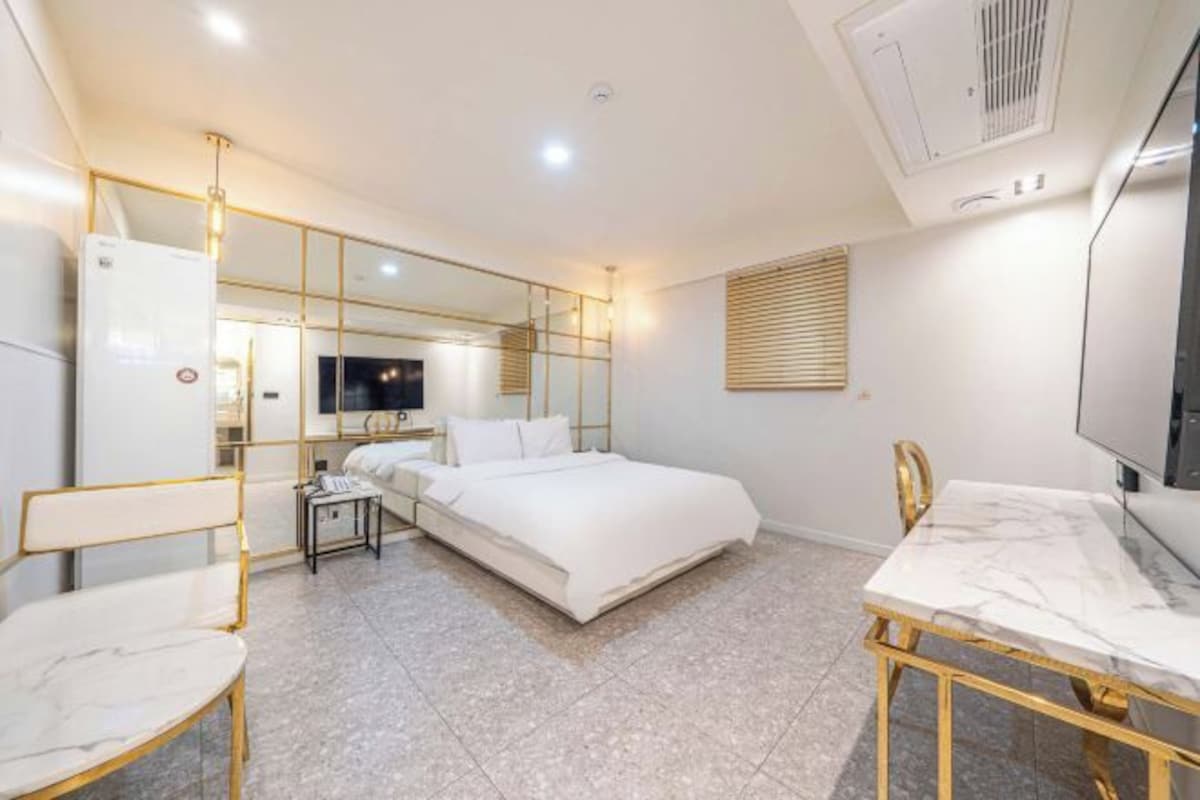 Una habitación de hotel moderna con una cama, un escritorio y una silla. Hay un televisor en la pared y una ventana con persianas.