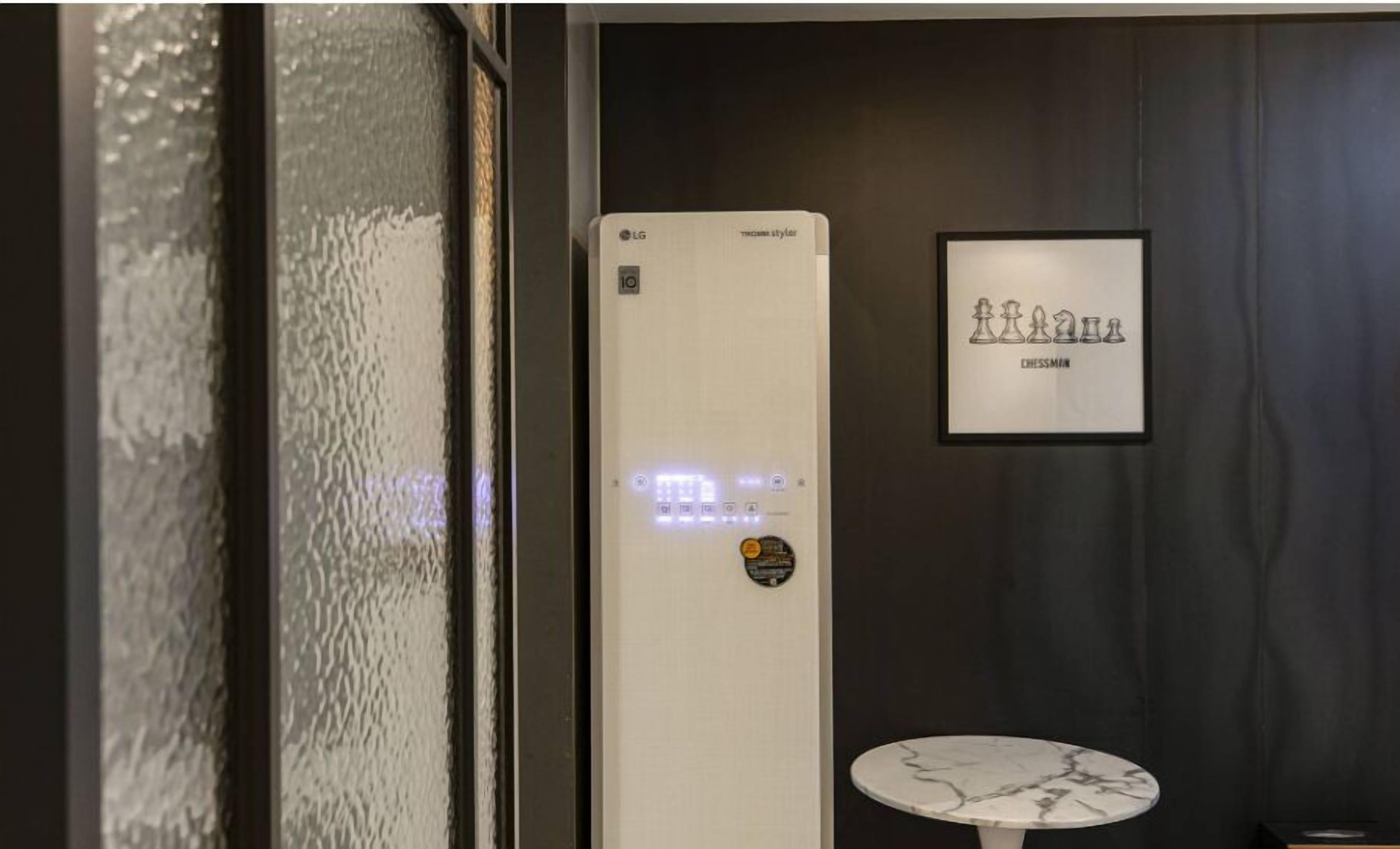 Una habitación con un termostato blanco instalado en la pared, un tablero de ajedrez enmarcado y una pequeña mesa redonda.