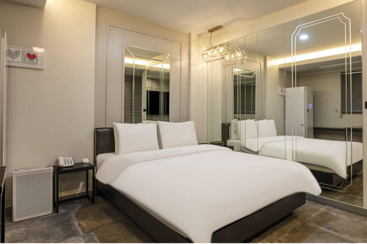 A modern hotel room with a large bed, a bedside table, a mirror, and a wardrobe.