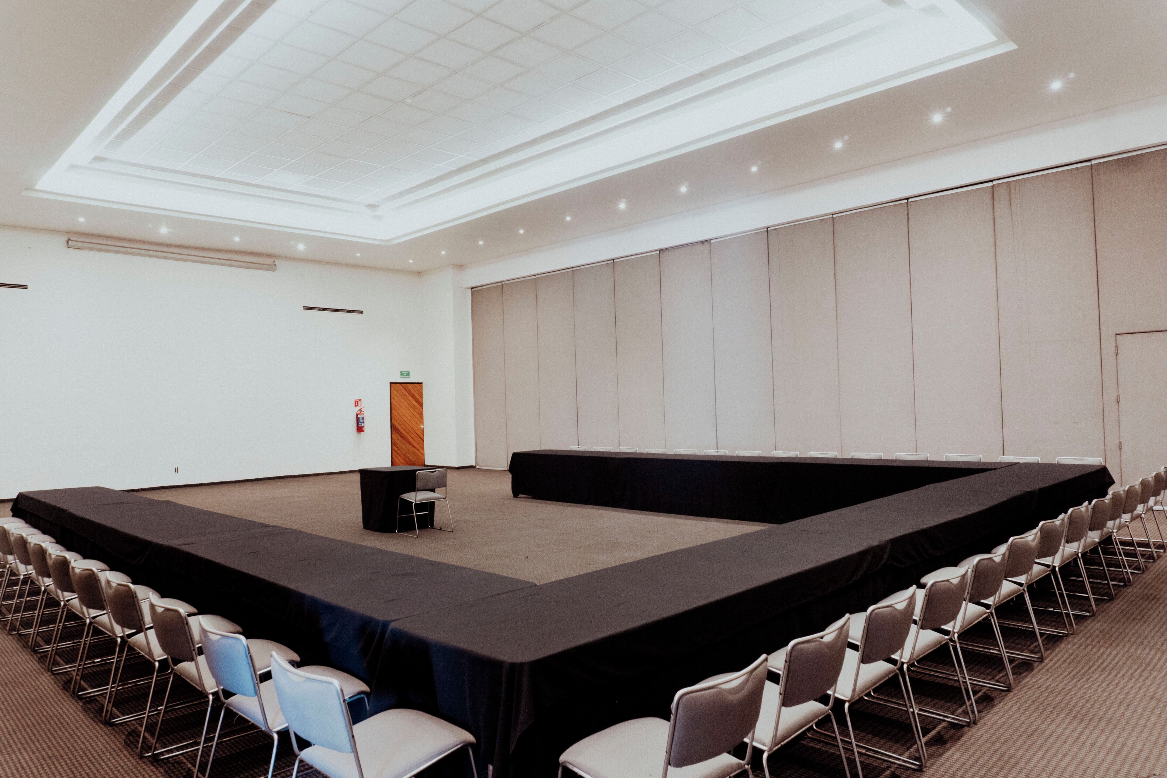 A conference room with a stage, rows of chairs, a podium, and a ceiling with recessed lighting.