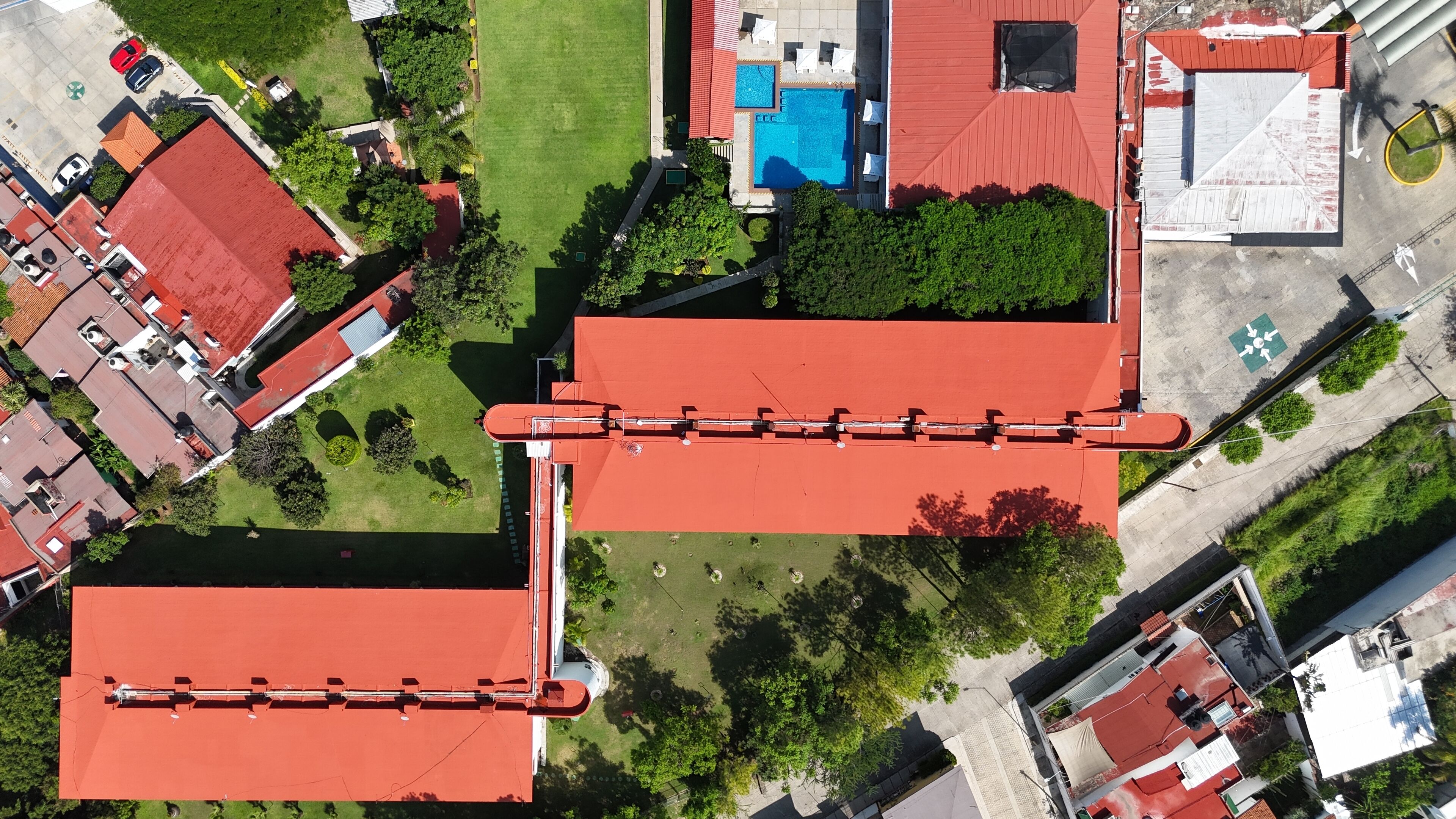 An aerial view of a residential area with red-roofed buildings, a swimming pool, and green spaces.