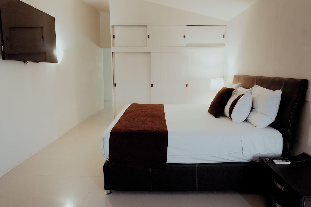 Een moderne slaapkamer met een groot bed, een aan de muur bevestigde televisie en een garderobe met meerdere deuren.