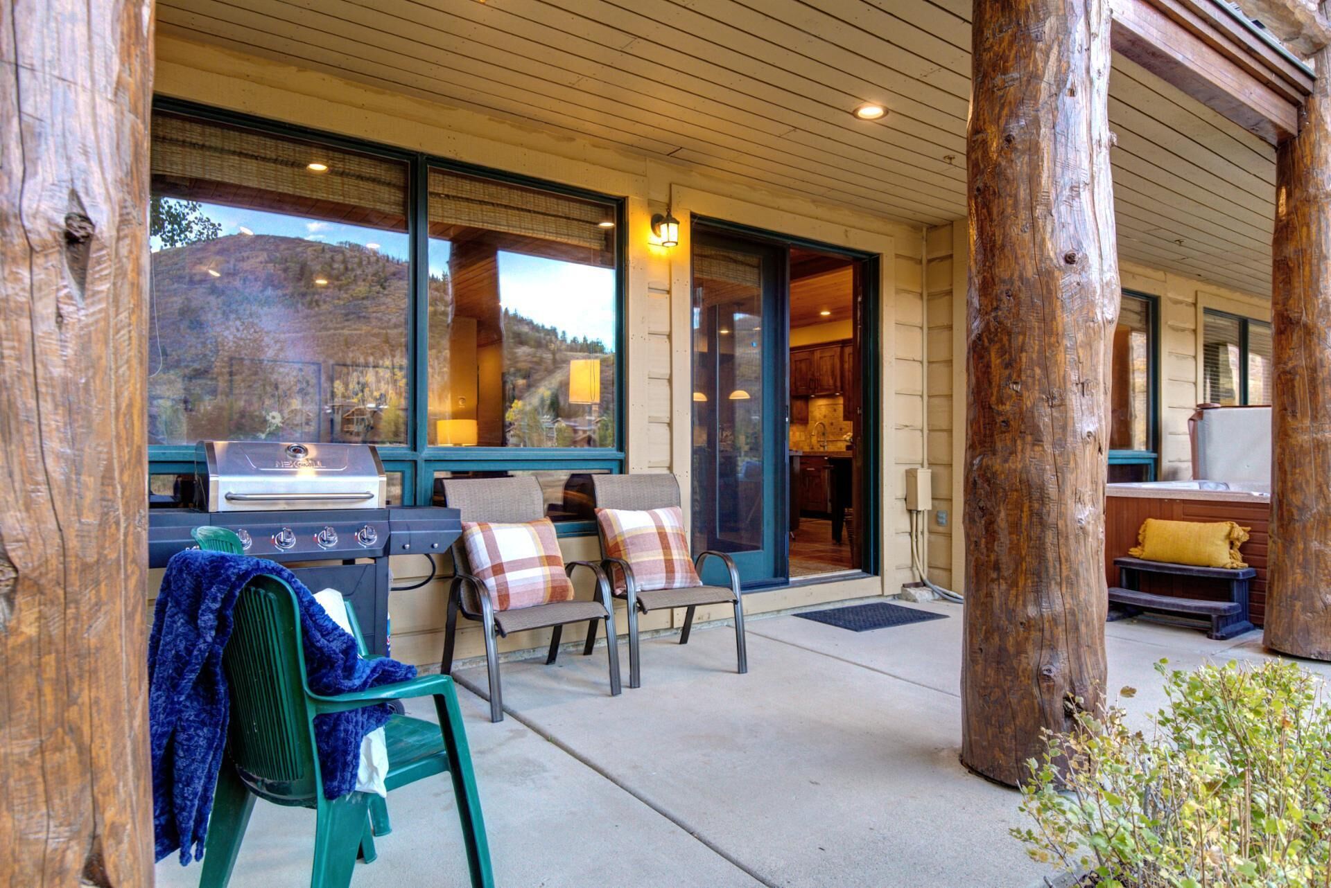 A covered outdoor seating area with a grill, two chairs, and a bench.