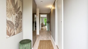A hallway with a green ottoman, a woven rug, and a large floral artwork on the wall.