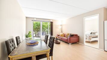 A modern living room with a dining area, featuring a marble table, leather chairs, a red sofa, and a large sliding glass door leading to a balcony.