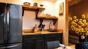 A modern kitchen with a stainless steel refrigerator, wooden countertop, and black cabinets. There is a dining table with plates and a vase of yellow flowers. - Biggest Deck! Beautiful Dome (Pikeville)