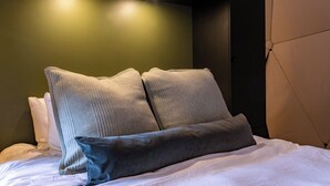 Een net opgemaakt bed met witte lakens en twee grijze kussens.