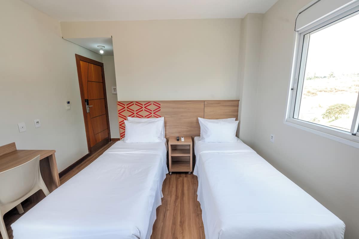 A hotel room with two single beds, a wooden headboard, a small bedside table, a desk, and a chair.