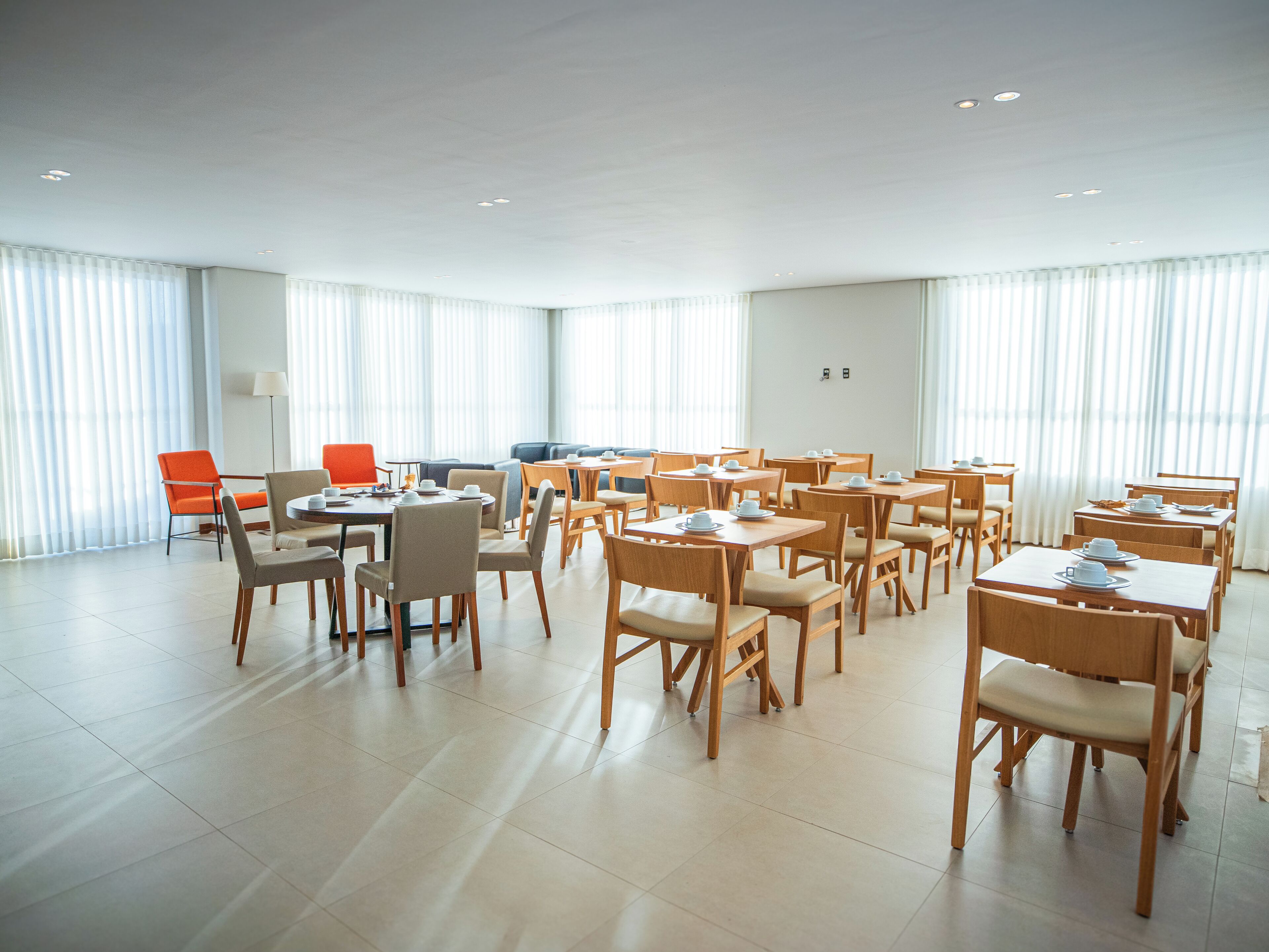Un comedor amplio con varias mesas y sillas, ventanas grandes con persianas y un interior moderno y pulcro.