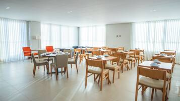 Un comedor amplio con varias mesas y sillas, ventanas grandes con persianas y un interior moderno y pulcro.