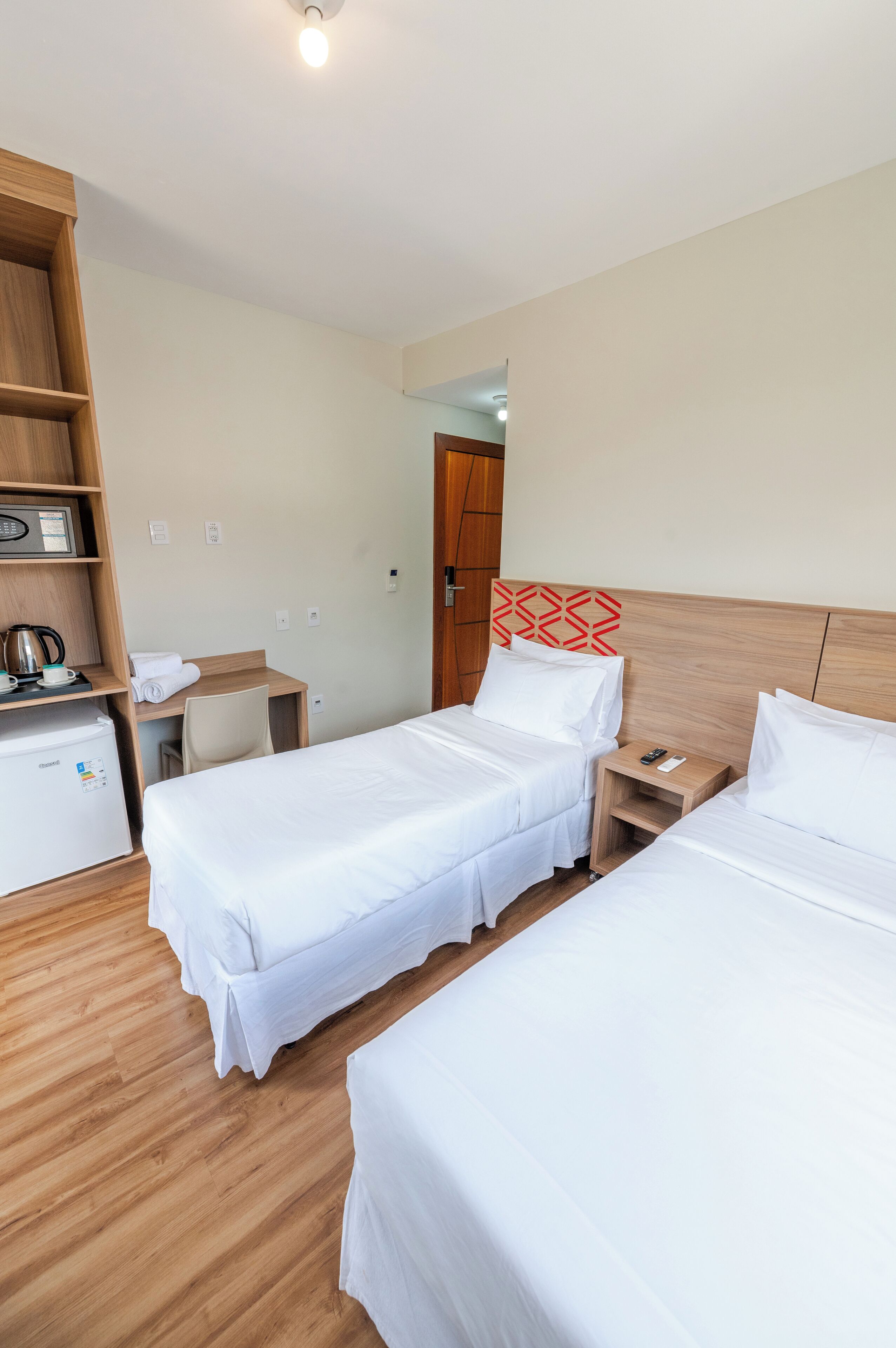 A hotel room with two single beds, a desk, a chair, a small refrigerator, and a microwave.