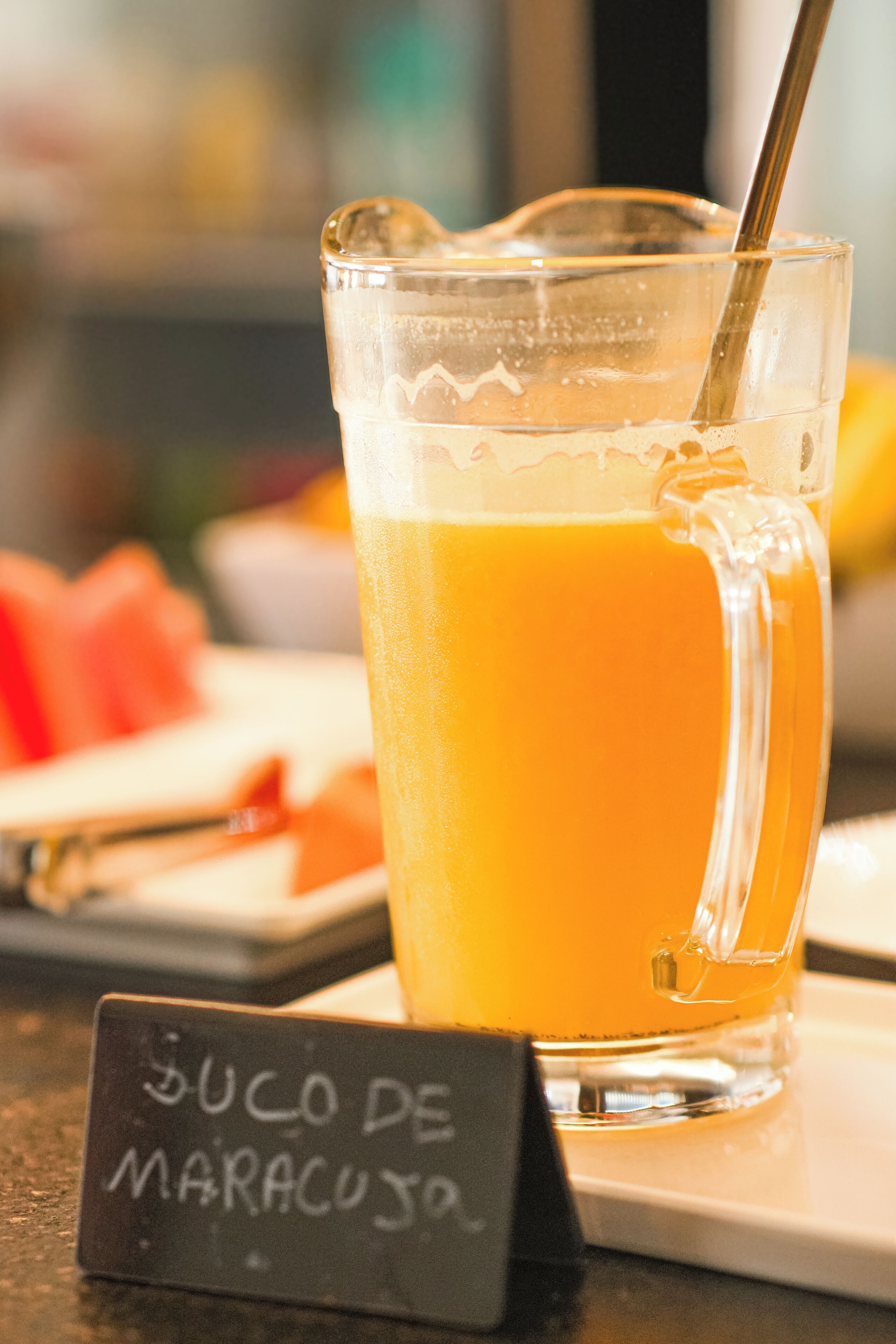 Un verre de jus d’orange avec une paille, posé sur une table à côté d’un panneau indiquant « Suco de Maracujá ».