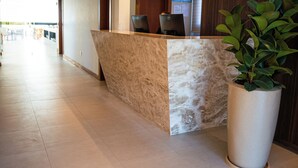 Een receptiezone met een marmeren balie, twee computerwerkplekken, een grote kamerplant en een wand van houten panelen.