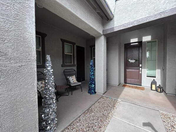 A covered outdoor area with a small Christmas tree, a bench, and a door with a wreath.