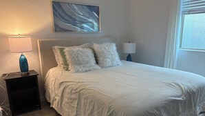 A neatly made bed with white bedding, two fluffy pillows, and a blue vase on a bedside table.