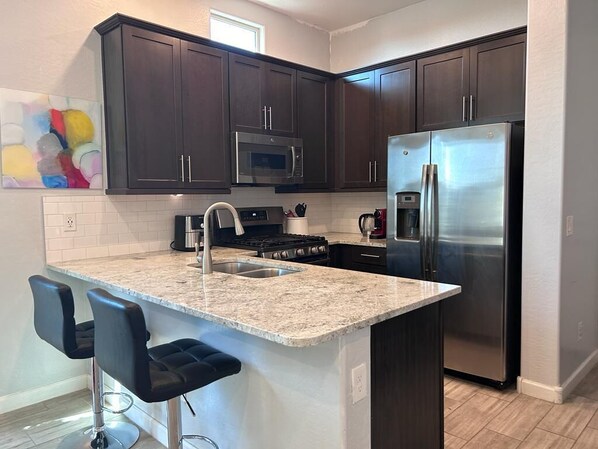 A modern kitchen with dark wood cabinets, stainless steel appliances, a granite countertop, and two bar stools.