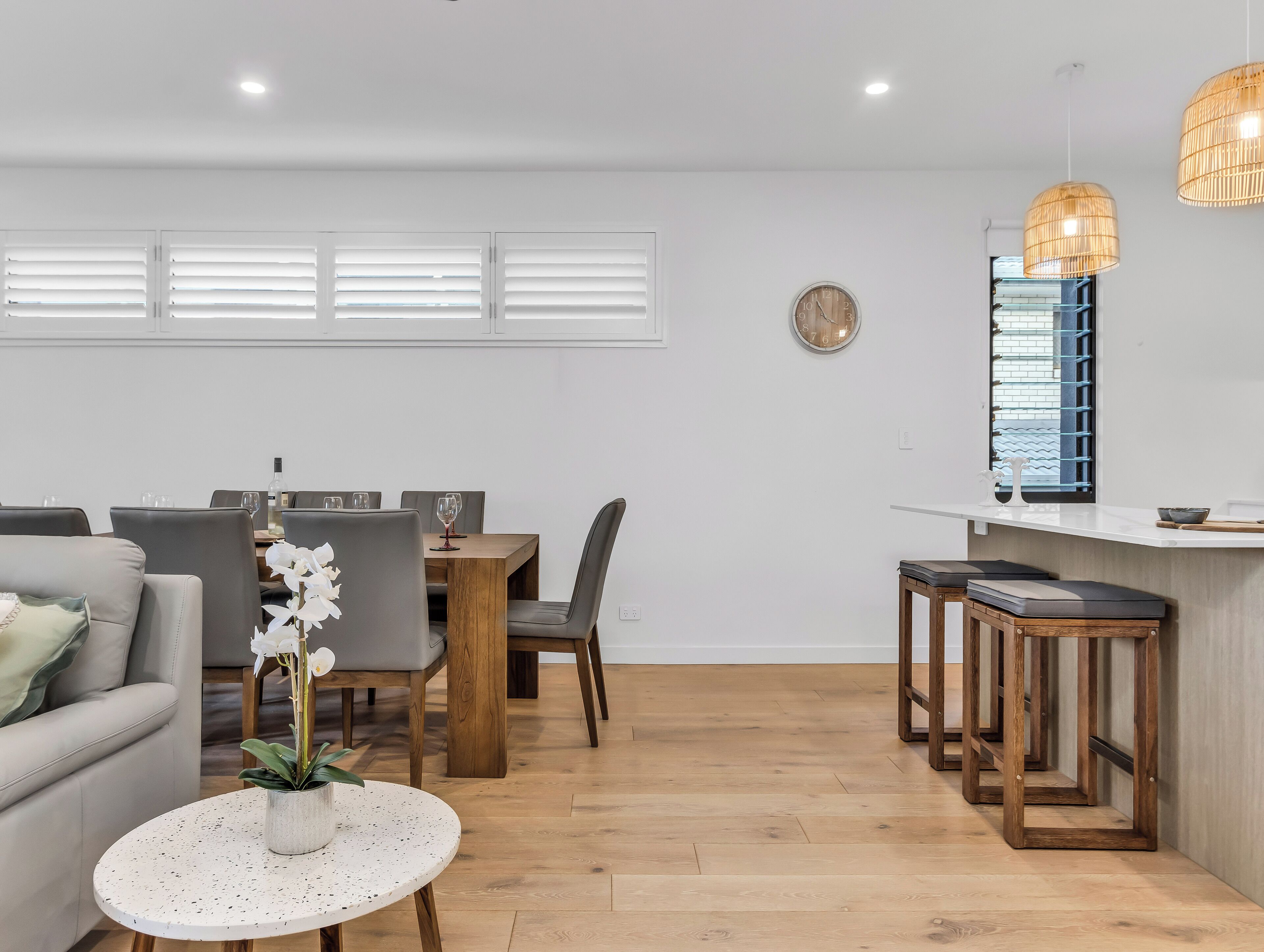 A modern living room with a dining area, wooden flooring, a round coffee table with a plant, and a kitchen counter with stools.