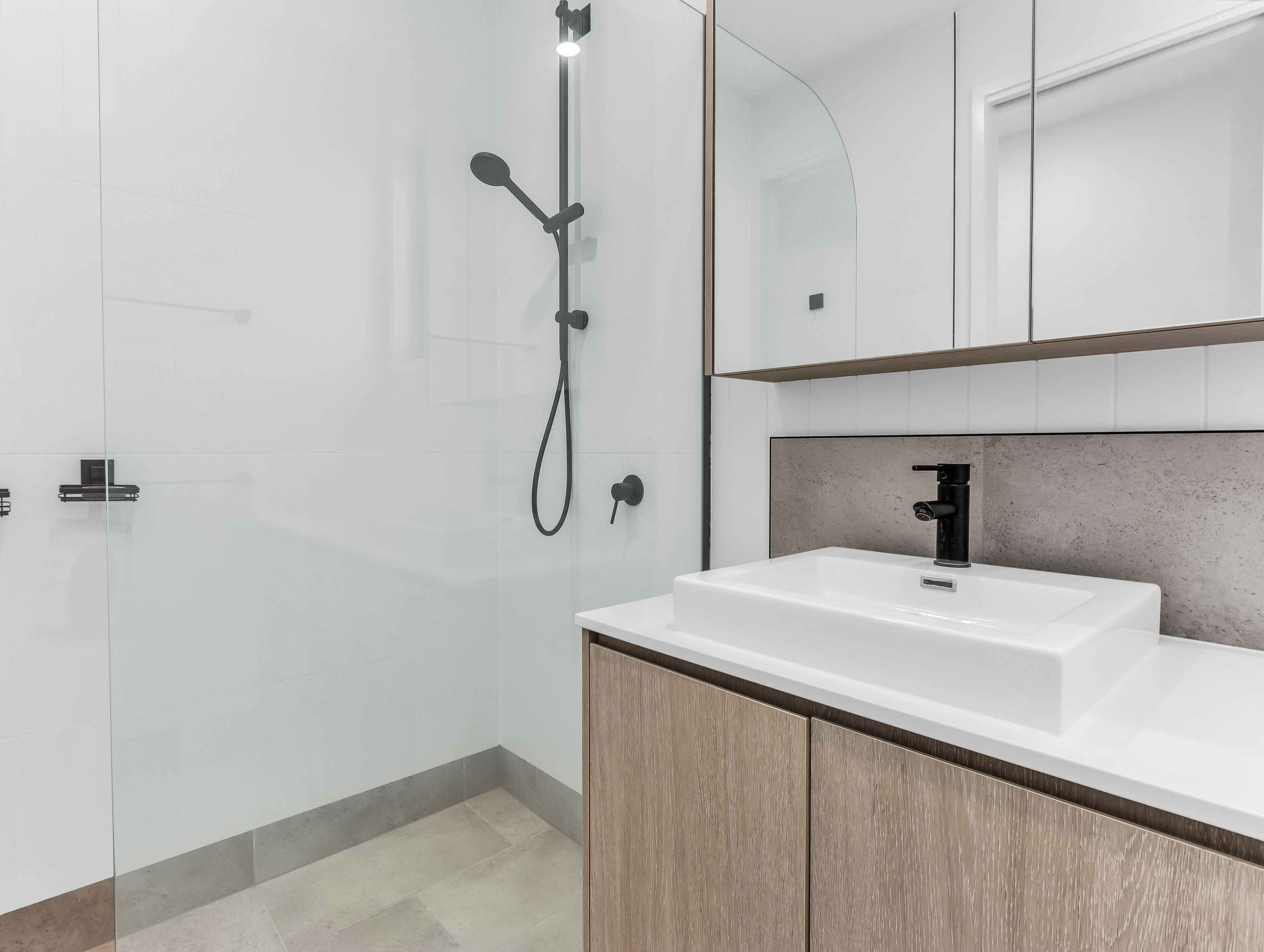 Une salle de bain moderne avec une douche à parois de verre, un lavabo blanc et des meubles en bois.