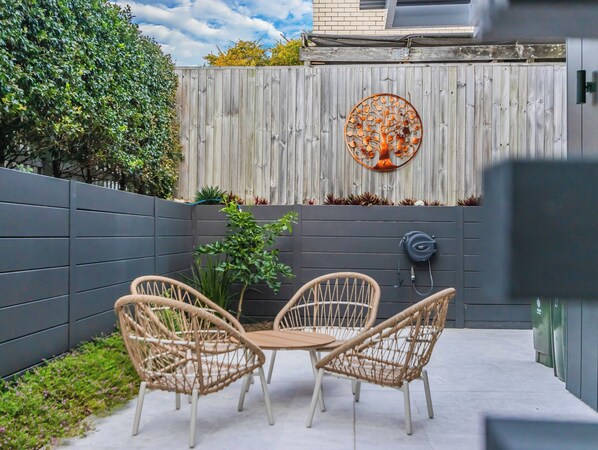 A patio with two wicker chairs and a table, a decorative metal tree, and a grey wall with plants. - Kingy Tidehouse (Kingscliff)