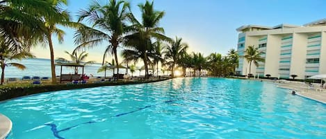 Una piscina con agua cristalina azul, rodeada de palmeras y un edificio de hotel.