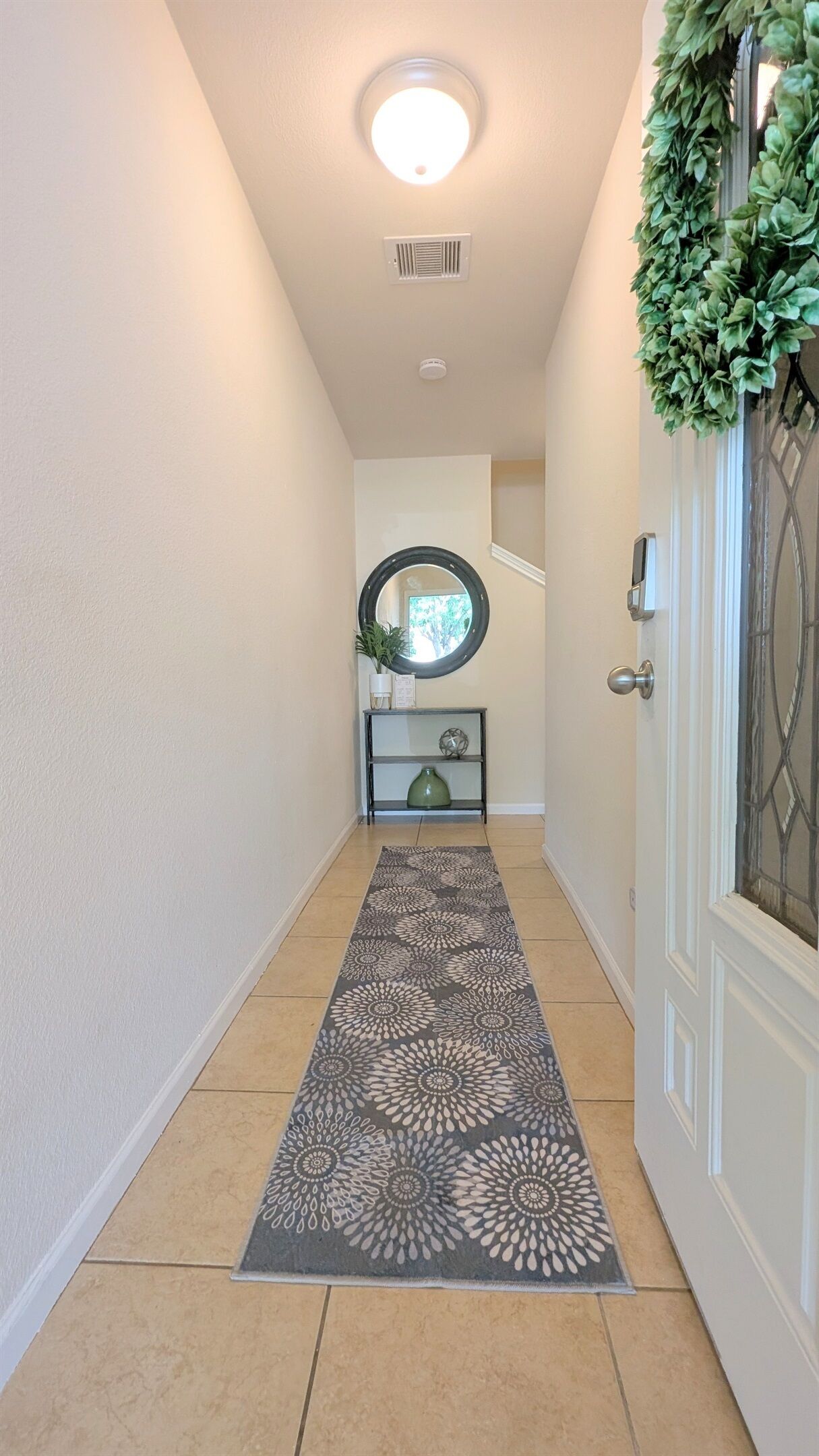 Un couloir avec un tapis à motifs, un miroir au mur et une porte ornée d’une guirlande décorative.
