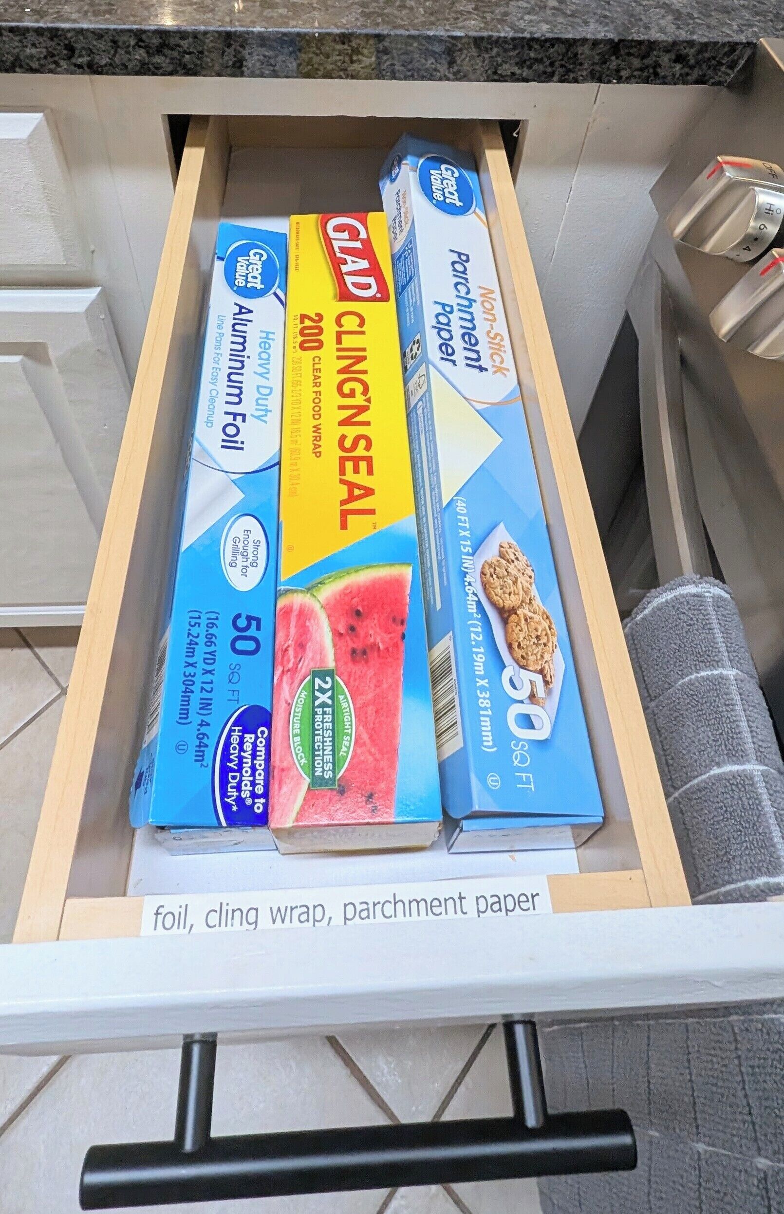 A drawer containing aluminum foil, cling wrap, parchment paper, and a box of parchment paper.