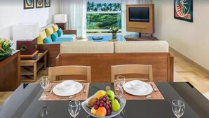 Un comedor con una mesa dispuesta para cuatro personas, un frutero en el centro y vistas al exterior a través de una ventana.