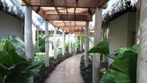 Un sendero de madera bordeado de grandes plantas tropicales y una estructura cubierta con techos de paja.