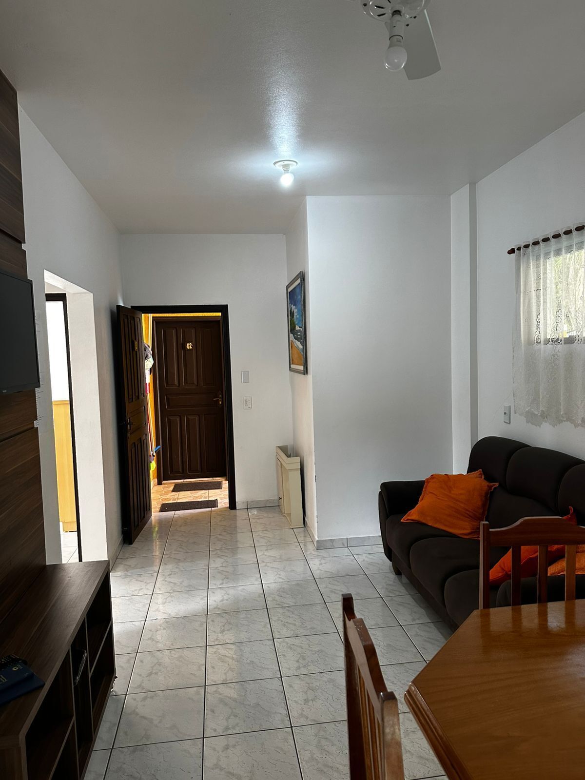 A spacious living area with a dark sofa, a wooden dining table, and a tiled floor.