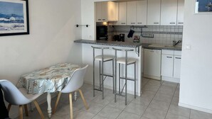A compact kitchen with a bar area, white cabinets, and a dining table with two chairs. - Sea-view apartment in Erquy | 4 guests | Ref 600 (ERQUY)