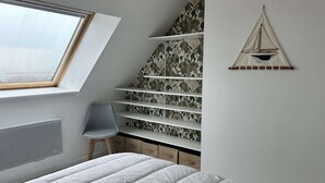 A bedroom with a sloped ceiling, a skylight, a bed, a chair, a shelf unit, and a wall-mounted sailboat decoration. - Sea-view apartment in Erquy | 4 guests | Ref 600 (ERQUY)