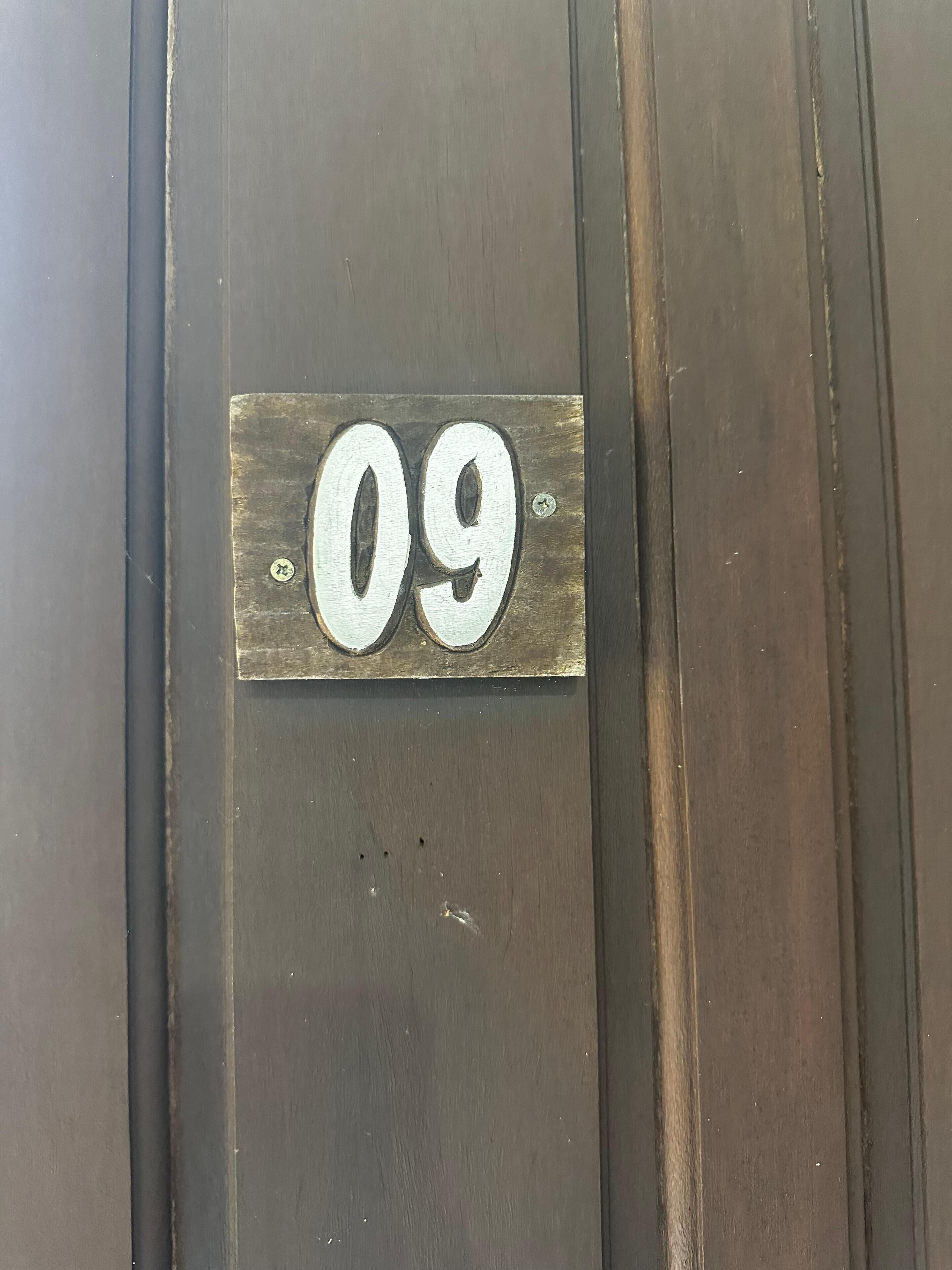 A metal number plate with the number 09 on a dark wooden surface.