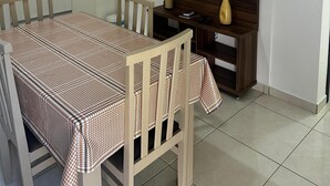 A small, clean room with a wooden accent wall, a flat-screen TV, a dining table with a checkered tablecloth, and a small shelf with decorative items. - Residencial Vista Bela Apt 09 (Two Suites) (Centro Bombinhas)