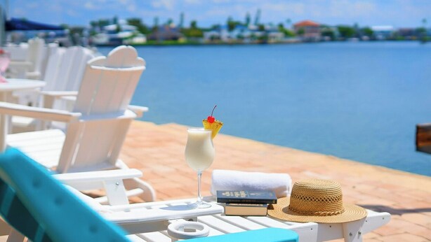 A beachside lounge with white lounge chairs, a drink with a cherry on the rim, and a straw hat on the table.