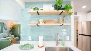 A modern kitchen with a stainless steel sink, wooden shelves, and a backsplash.
