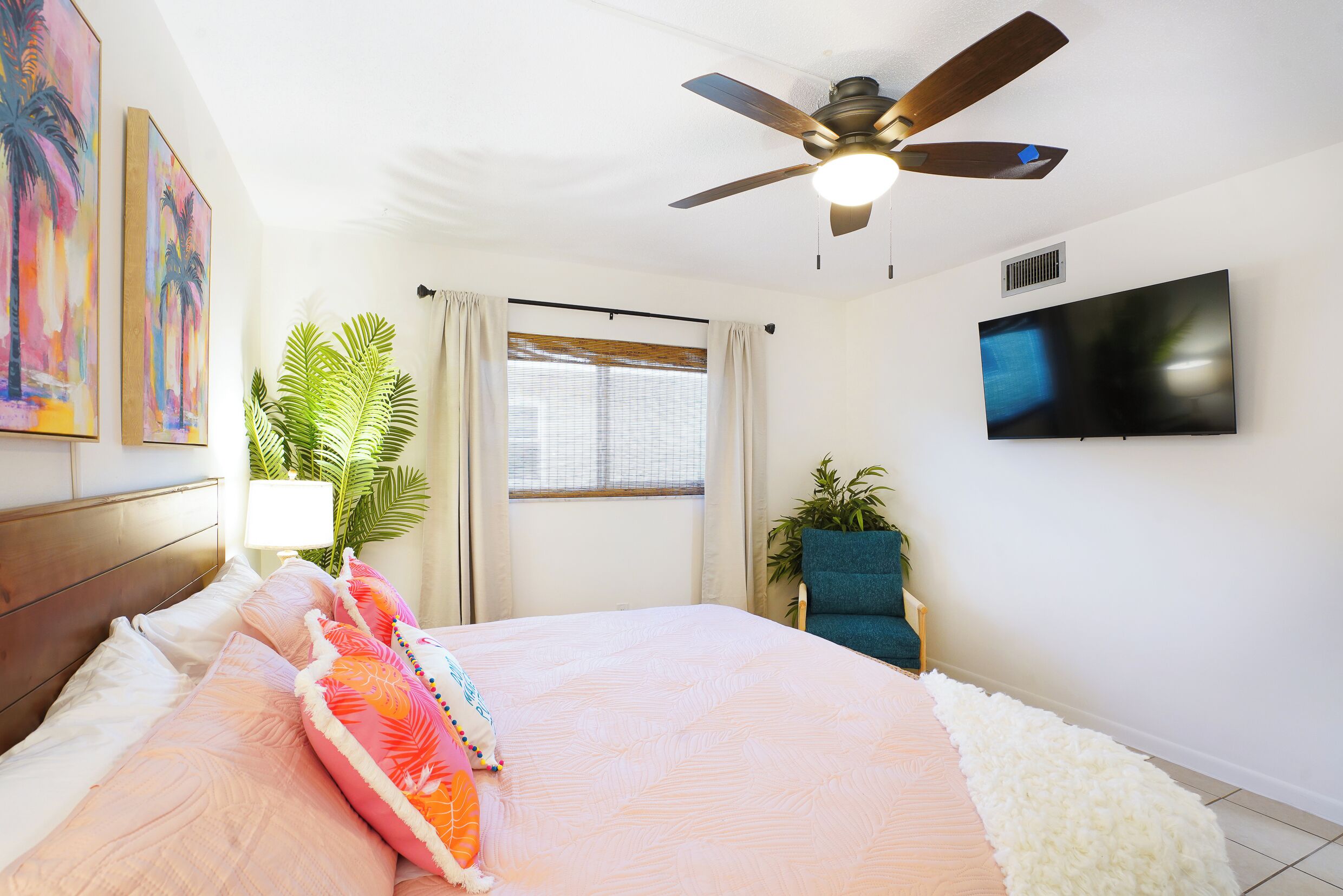 A bedroom with a bed, a ceiling fan, a TV, and a window with curtains.