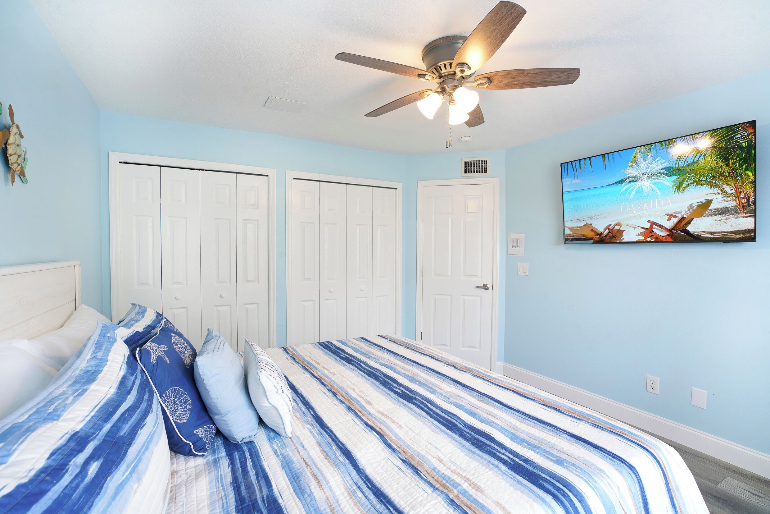 A bedroom with a bed, a ceiling fan, and a painting of a beach scene.