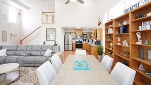 A spacious living area with a grey sectional sofa, a dining table with chairs, a ceiling fan, and a wooden bookshelf filled with decorative items. - Steps From Beach With 2 Golf Carts Sleeps 16! (Indian Rocks Beach)