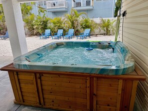 Ein Whirlpool mit Holzrahmen, umgeben von einer Terrasse mit Stühlen und Pflanzen.