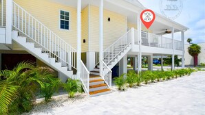 A two-story building with a white exterior, a covered porch, and a staircase leading to the second floor. - Steps From Beach With 2 Golf Carts Sleeps 16! (Indian Rocks Beach)