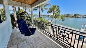 A balcony with a hanging chair, a view of a body of water, and palm trees. - Walk to Beach 5BR Wtr, Pool, Dock, Golf Cart (Indian Rocks Beach)