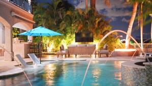 A swimming pool with lounge chairs and a TV screen, surrounded by palm trees and a tiled deck. - Walk to Beach 5BR Wtr, Pool, Dock, Golf Cart (Indian Rocks Beach)