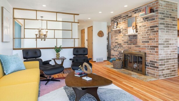 Ein modernes Wohnzimmer mit einem Kamin aus Ziegelsteinen, zwei schwarzen Ledersofas, einem gelben Sofa und einem Couchtisch mit Büchern.